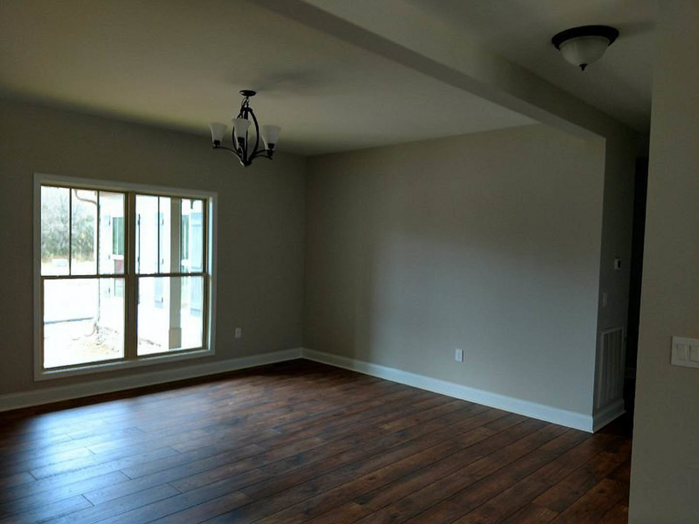 Dark hardwood floor in a room with white walls, large window with white frame, modern light fixture, and white light switch.