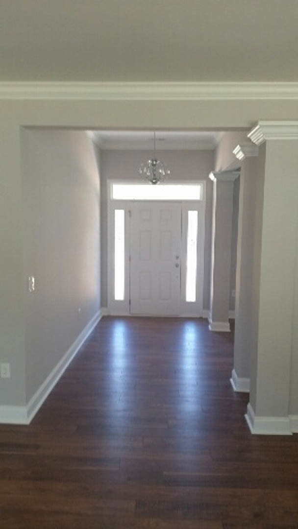 Hallway with dark wood flooring, white trim, white paneled door with window and white handle, chandelier overhead, plaster walls with molding