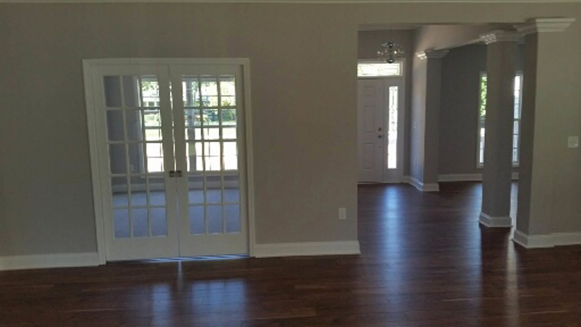 Double glass-paneled doors with white trim, wood laminate flooring, neutral walls, and natural light filtering through adjacent windows.