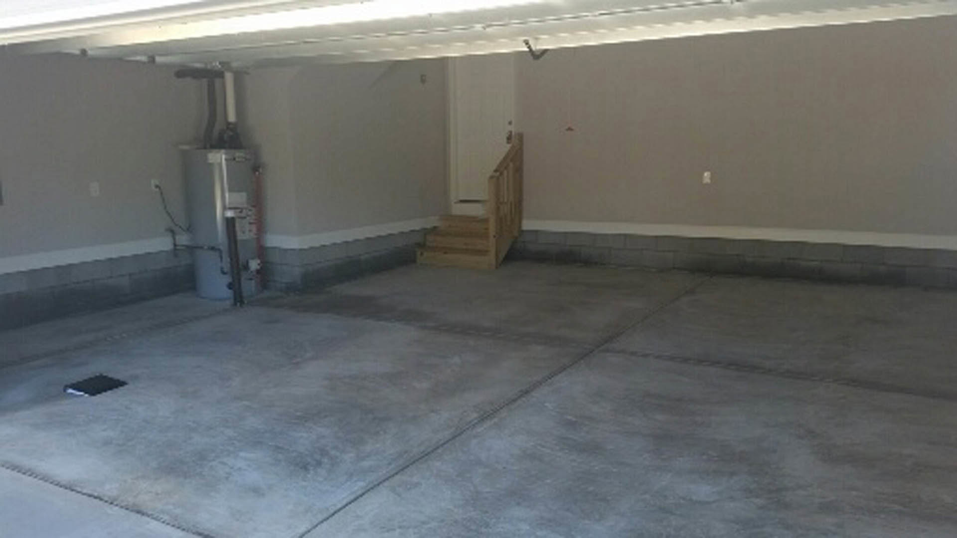 Garage interior with concrete floor, white plaster walls, staircase leading upward, and tile flooring near entry.