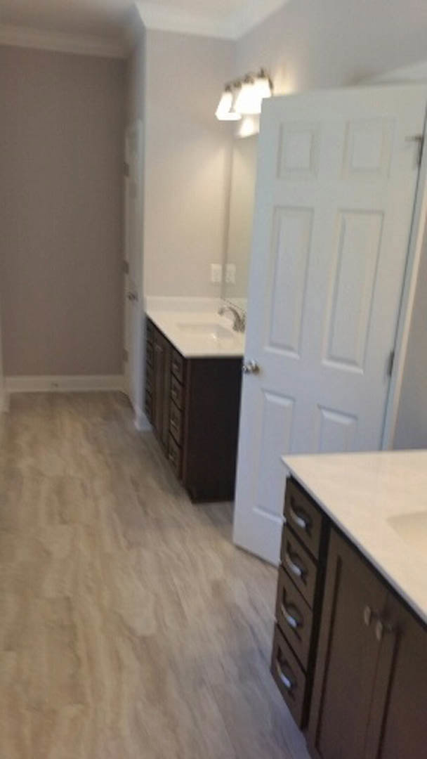 Bathroom with wood flooring, white door featuring silver knobs, white countertop and sink, cabinetry with drawers, and light-colored walls.