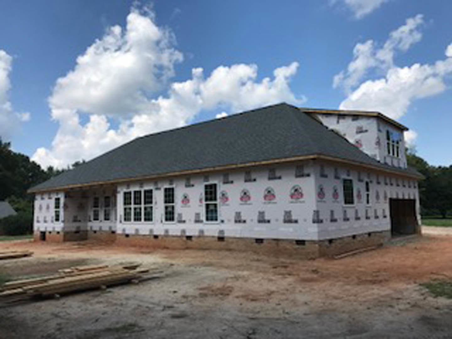 Modern home under construction with large windows, unfinished exterior walls, and a pitched roof beneath a clear blue sky