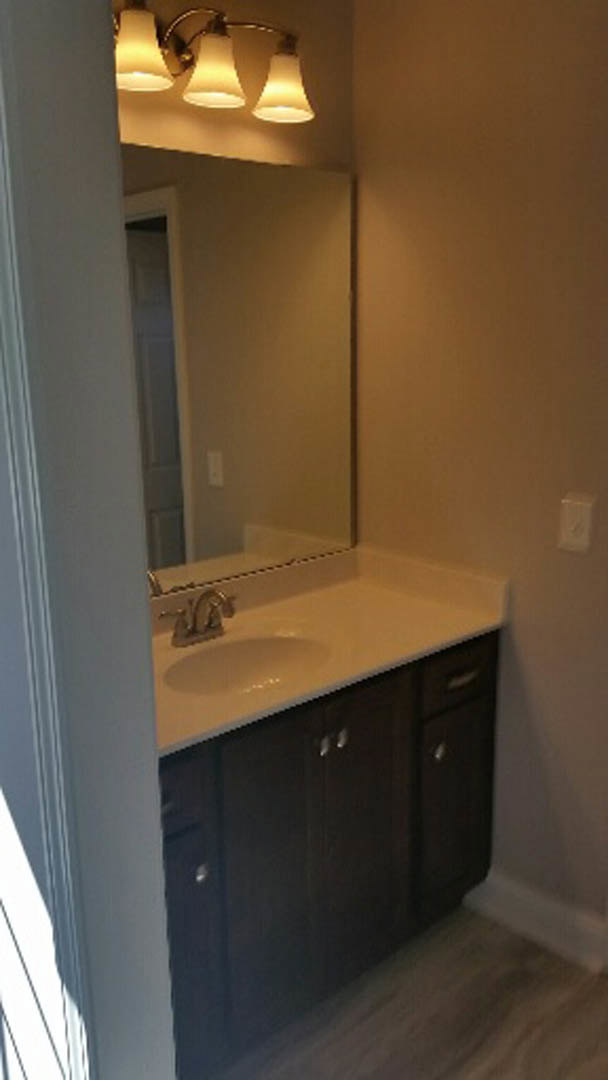 White bathroom vanity with quartz countertop, rectangular undermount sink, chrome faucet, large framed mirror, light gray tile backsplash, and shaker-style cabinetry with brushed