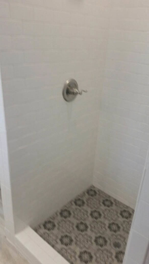 Patterned tile floor and marble shower wall with chrome handle in modern bathroom.