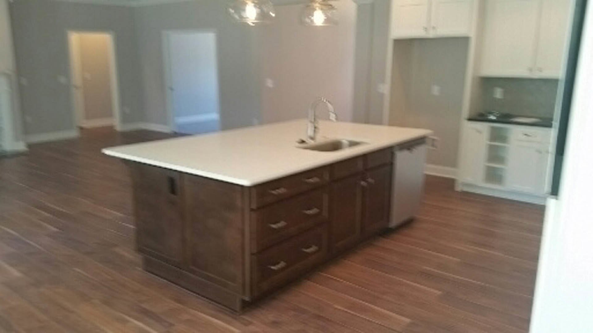 Kitchen island with built-in sink, white tile backsplash, wood cabinetry, stone countertop, and drawers on hardwood floor