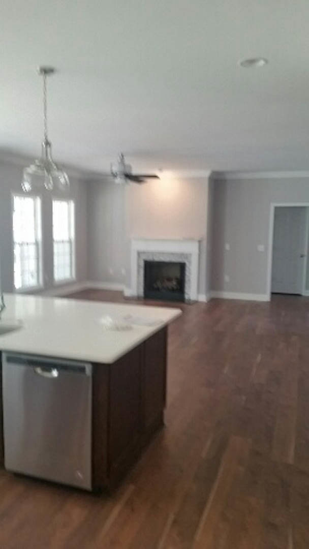 Open concept living room with tile flooring, stone fireplace, and adjacent kitchen featuring white cabinetry, stainless steel dishwasher, and marble countertops
