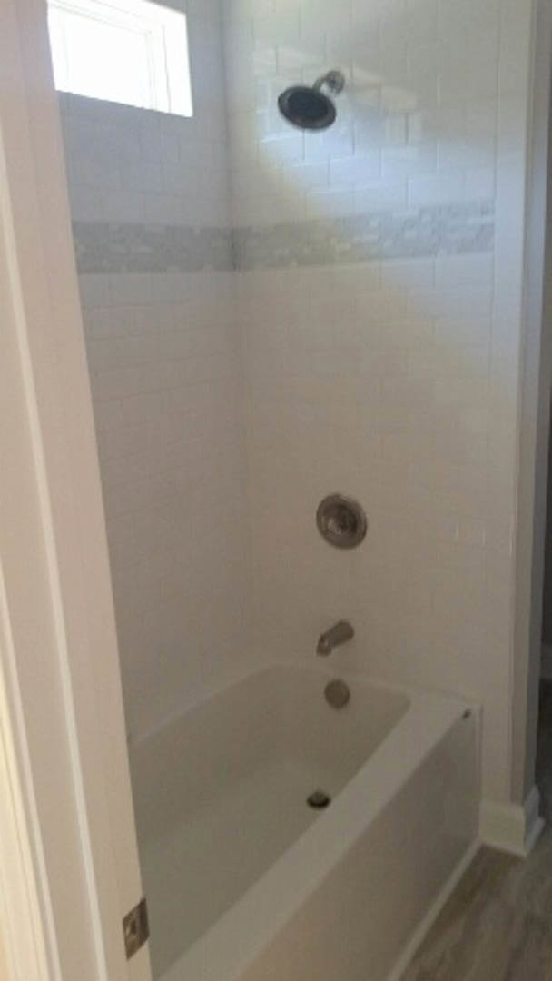 Freestanding white bathtub with chrome faucet set against light tile wall in modern bathroom