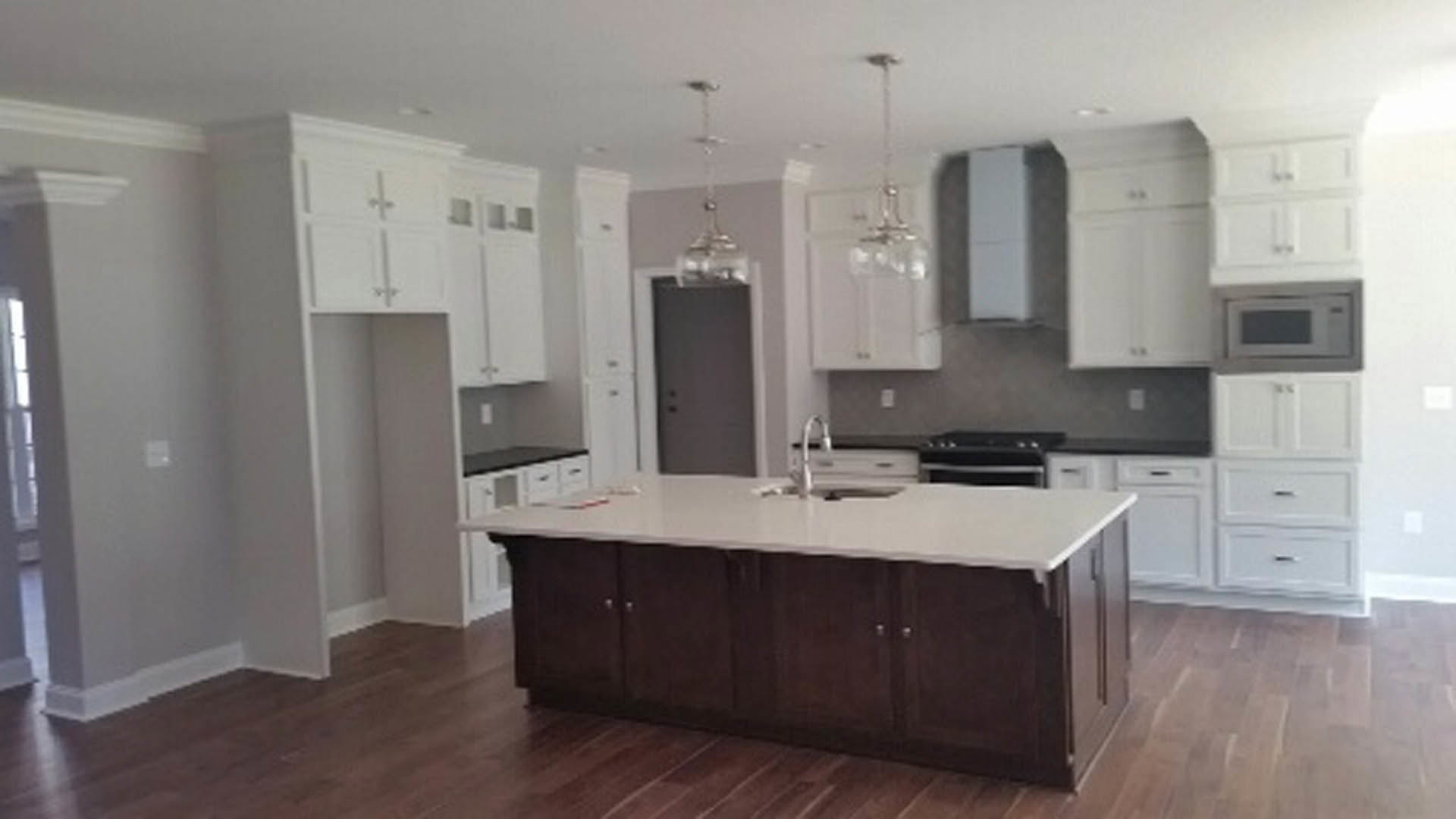 Spacious kitchen featuring a large central island with white quartz countertop, light wood cabinetry, stainless steel sink, and built-in appliances