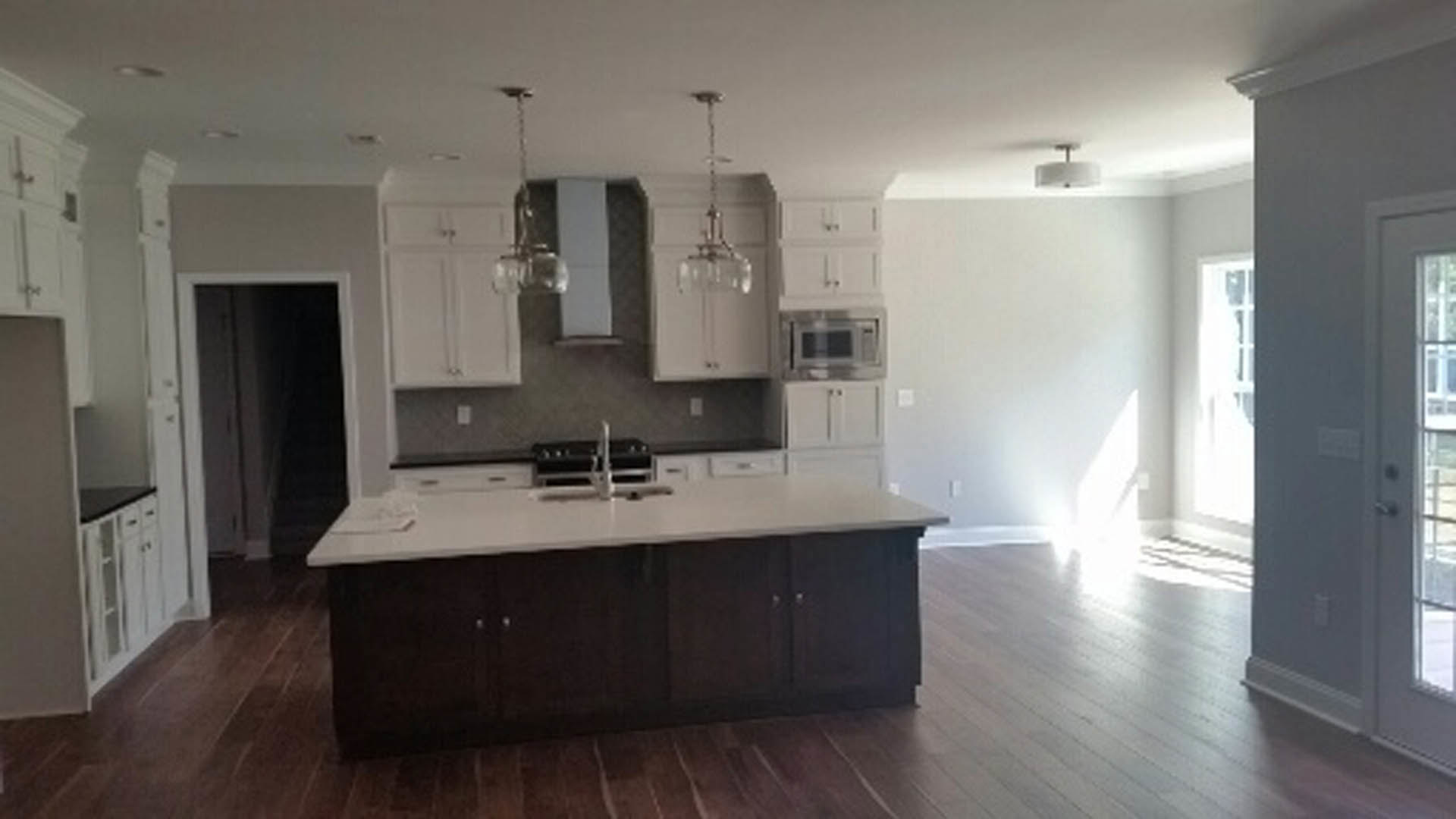 Kitchen with wood flooring, central island featuring stone countertop, white cabinetry, stainless steel sink, and tile backsplash