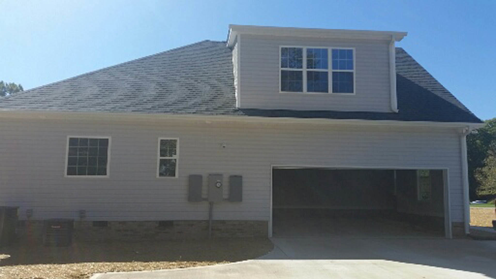 Two-story home with gray siding, white trim, attached two-car garage, large windows, and landscaped front yard with mature trees