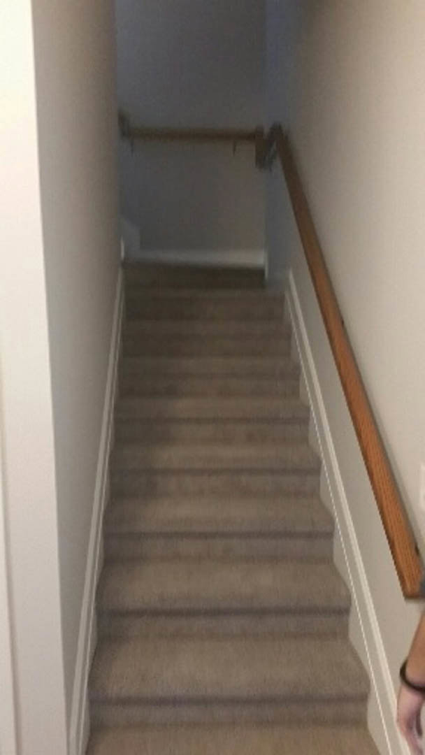 Wood staircase with metal handrail beside an open white door, plaster walls, and light hardwood flooring