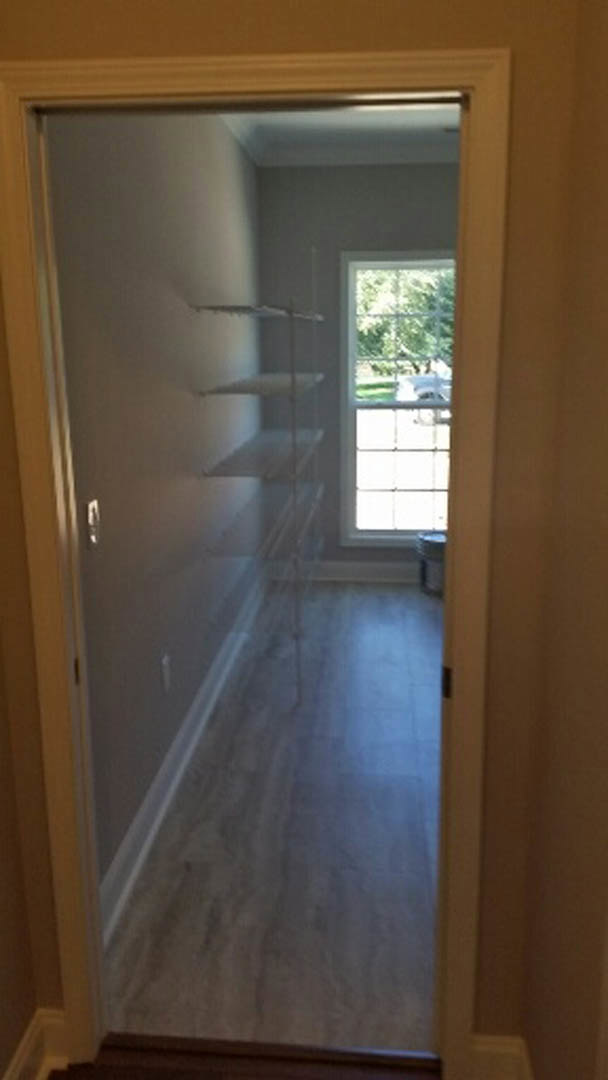 Wood-floored room featuring a large window with a view of a parked car outside, white walls, and modern door hardware