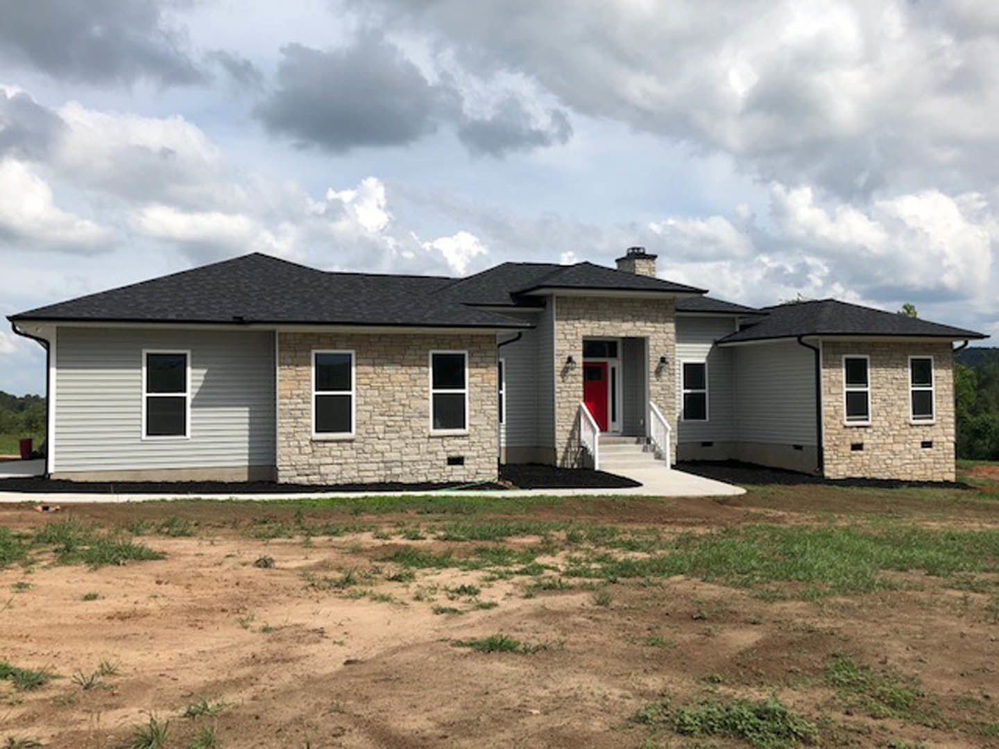 White cottage-style home with red door featuring glass panes, white-framed windows, brick chimney, grassy dirt yard, cloudy sky, and a blurry red and black sign near the entrance