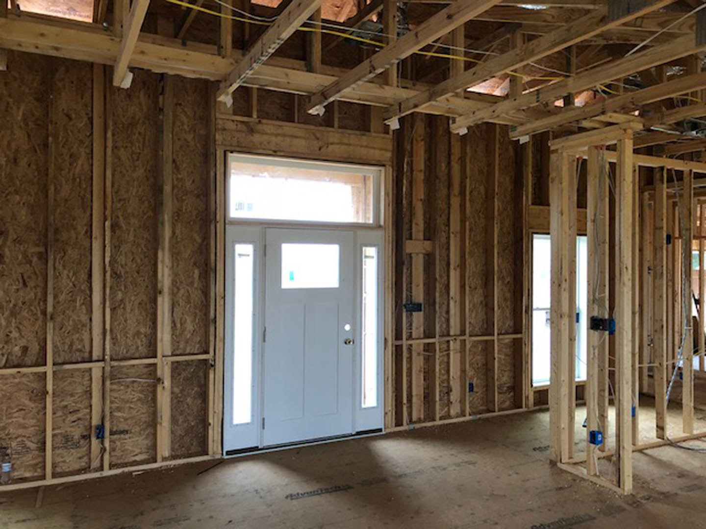 Wood-framed interior under construction with exposed beams, unfinished flooring, and a white door featuring a window panel