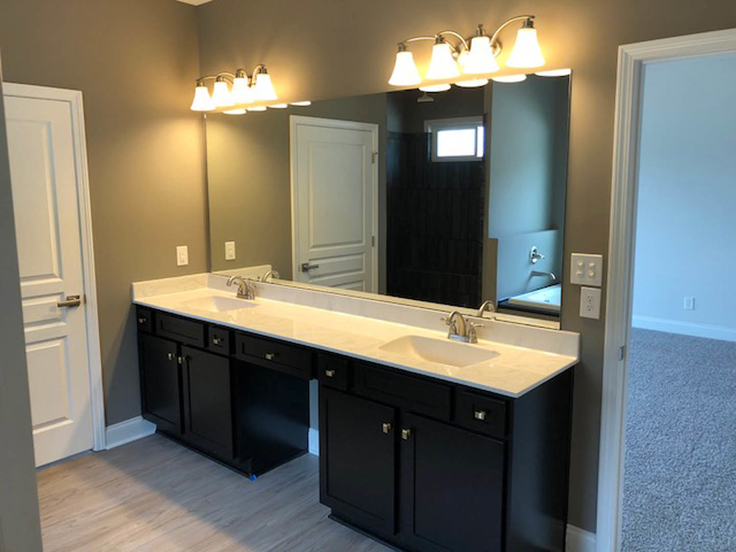 Bathroom with expansive wall mirror, double white sinks set in a stone countertop, modern chrome faucets, light wood cabinetry, neutral tile flooring, and minimalistic accessories
