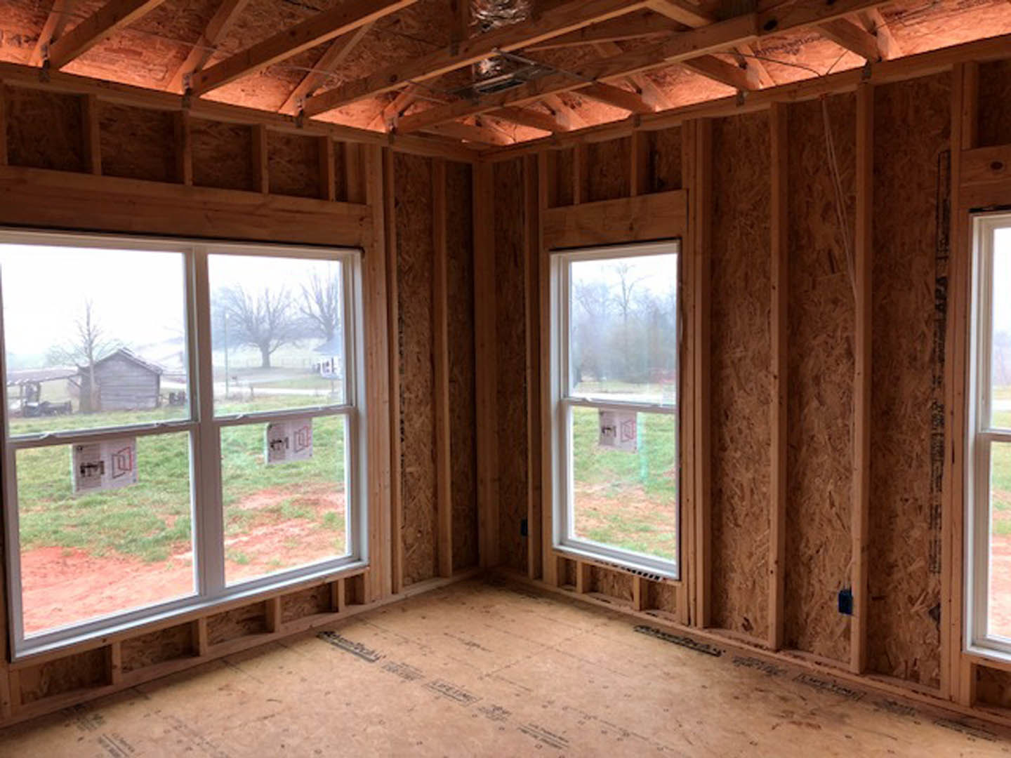 Spacious room featuring large windows, exposed wood ceiling beams, wood plank flooring, and wood-paneled walls.