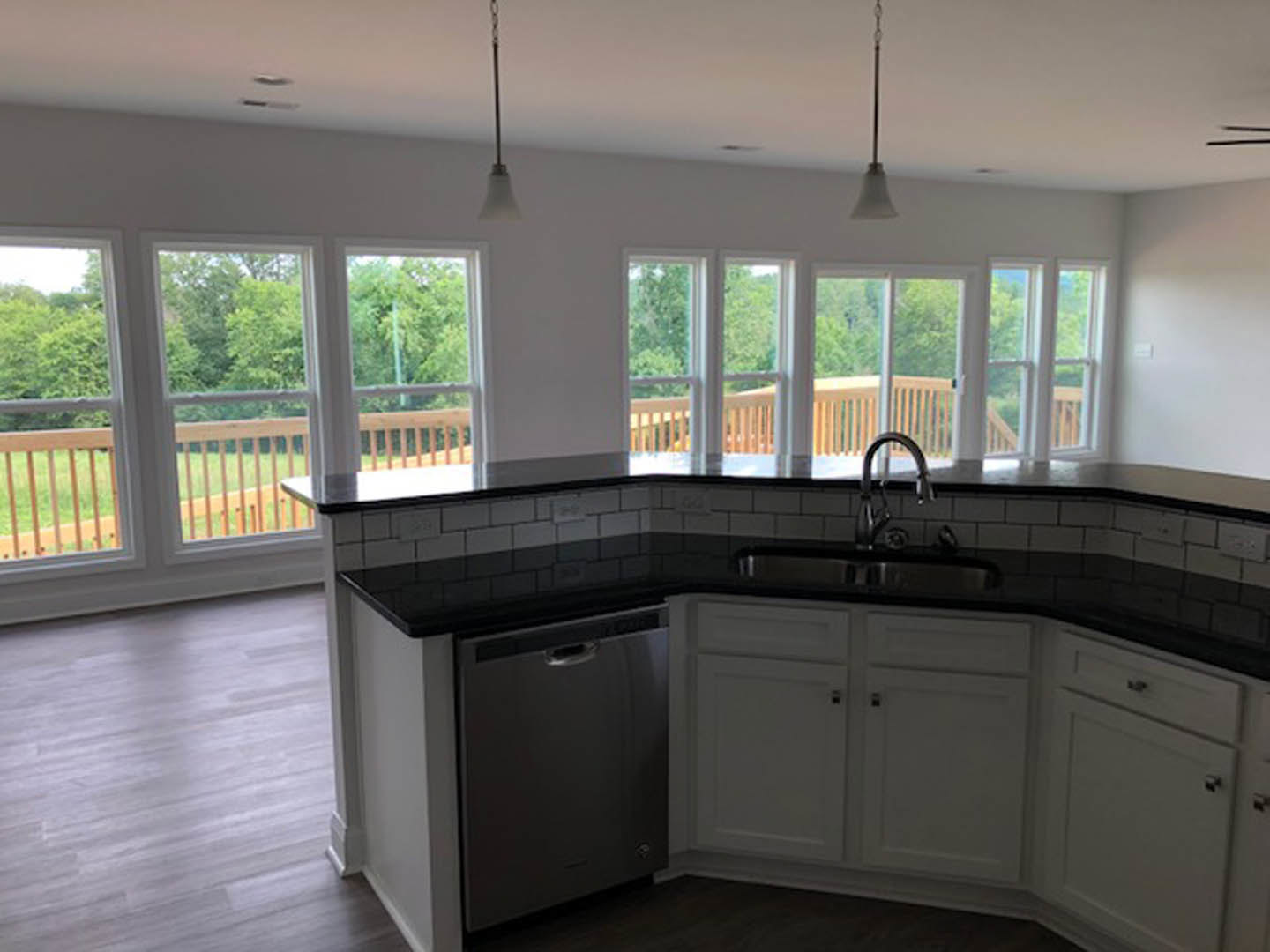 Bright kitchen featuring a large window above the sink, white cabinetry, stone countertops, and wood flooring; a person's hand appears blurred in the foreground.