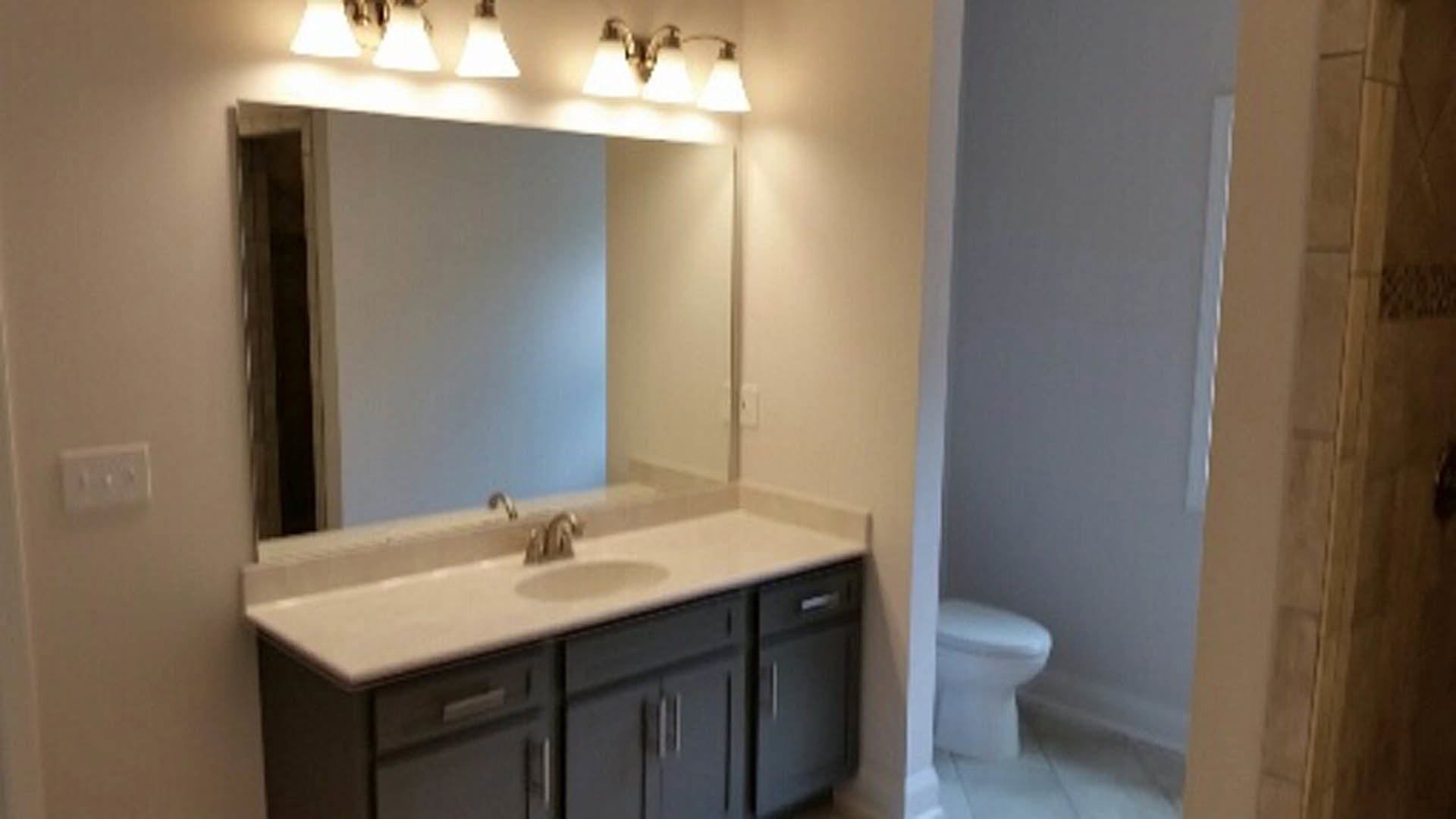 Modern bathroom featuring white ceramic sink with chrome faucet, matching toilet, light gray tile walls, wood vanity cabinetry, and quartz countertop