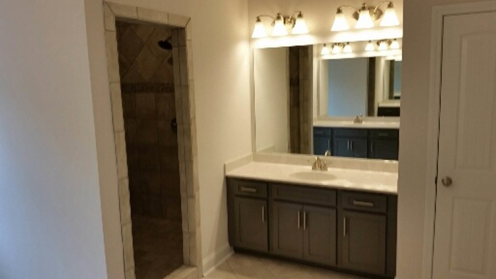 Modern bathroom featuring a glass-enclosed shower, white ceramic sink with chrome tap, light tile walls, and wood cabinetry with drawers.