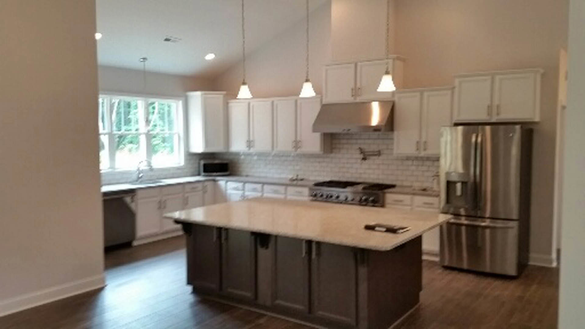 Spacious kitchen featuring a large central island with white countertop, tile backsplash, wood cabinetry, stainless steel appliances, and sink
