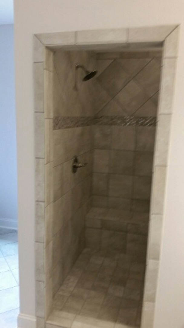 Marble tile shower with chrome shower head, white plaster walls, and tile flooring in modern bathroom