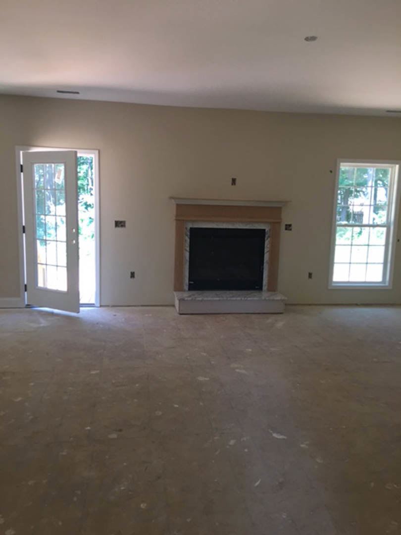 Living room with plaster walls, large windows overlooking trees, modern fireplace beneath a mounted black screen, hardwood flooring, and a staircase near a paneled door