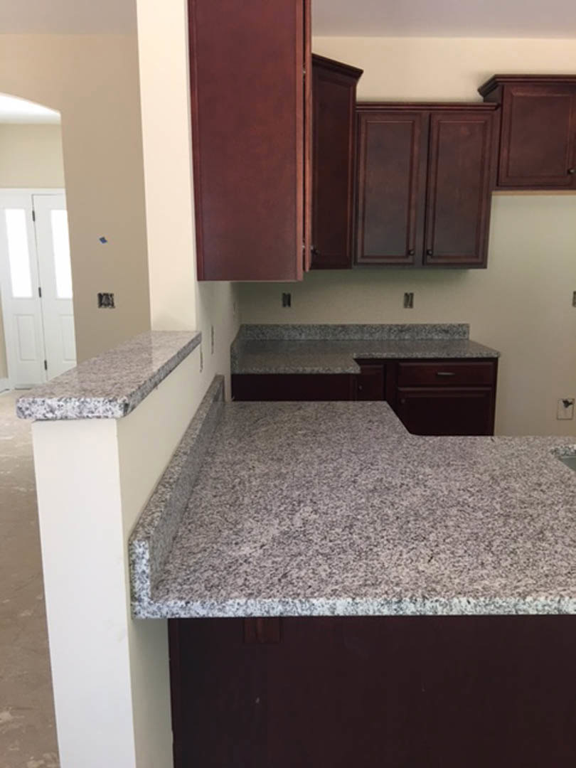 Granite countertops with dark wood cabinets, stainless steel sink, white tile backsplash, and a white door with black handle in a modern kitchen