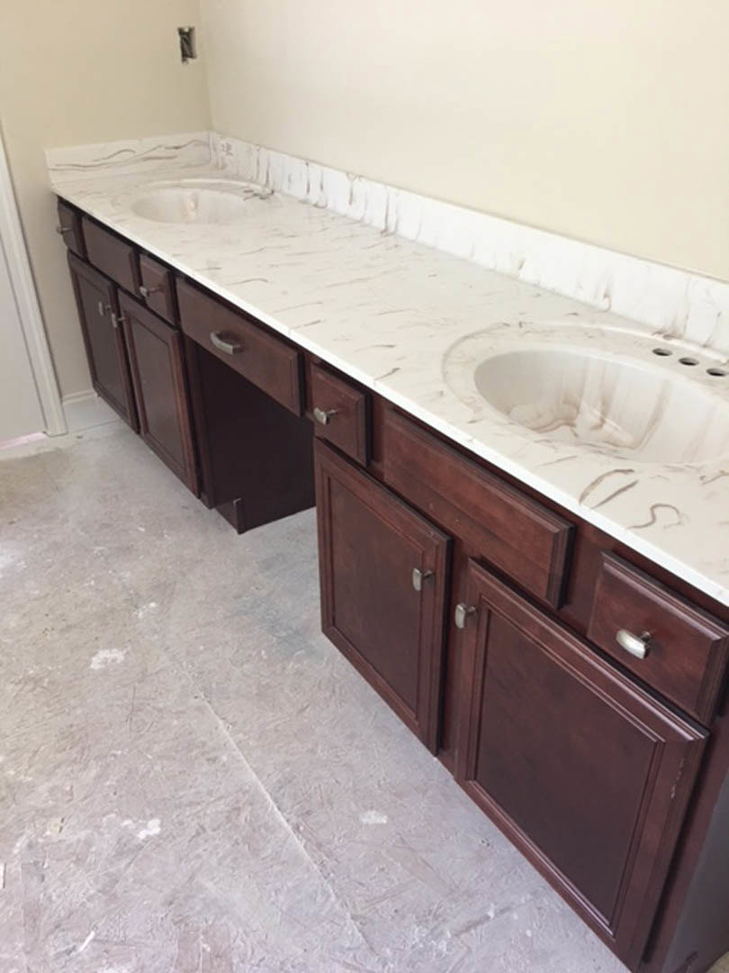 Bathroom with marble countertops, brown cabinets, white tile floor, white bathtub, chrome plumbing fixtures, and tile walls
