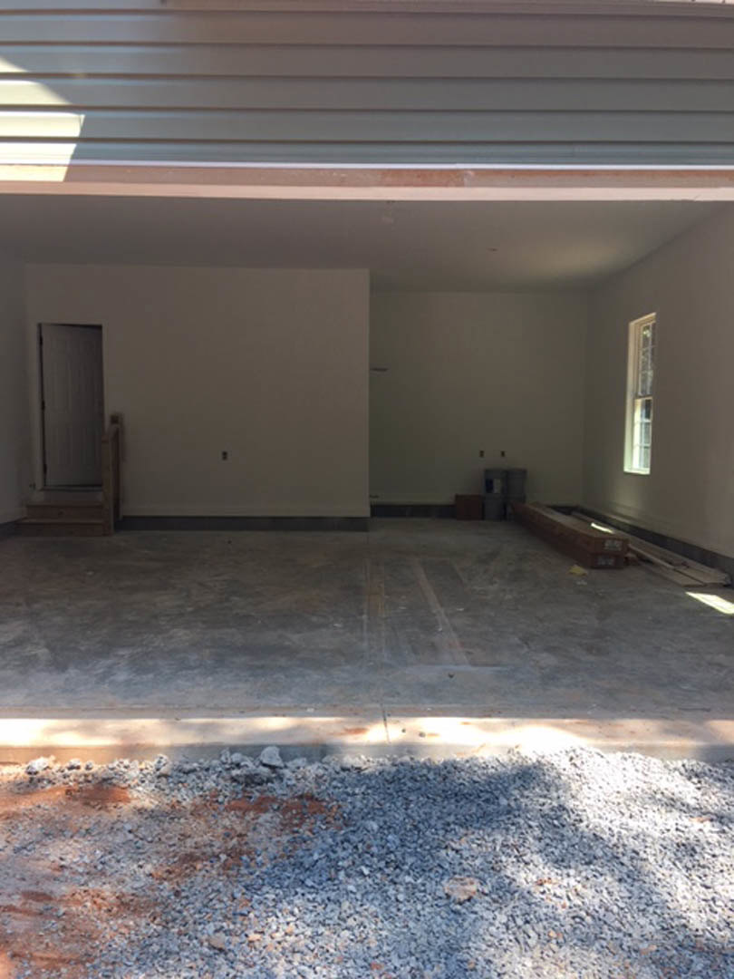 Concrete-floored room featuring a large glass garage door, white interior walls, ceiling with recessed lighting, pile of rocks near the entrance, white door with black trim, window