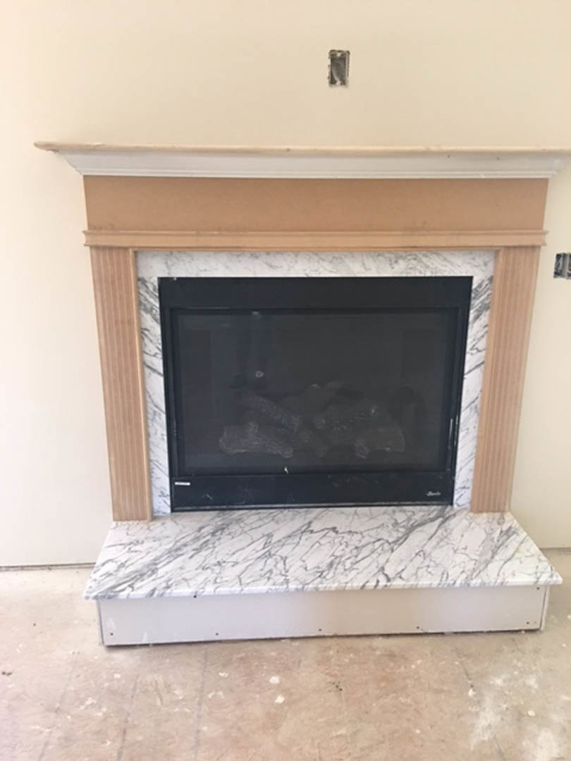 Stone fireplace surround with black glass-front insert, white countertop featuring subtle black veining, adjacent to brown tile flooring, close-up of textured stone surface.
