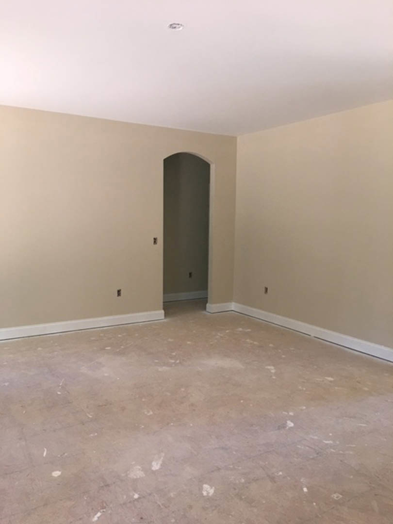 White door with matching frame open into living room; dirty floor with scattered white paint, faint white handprints on gray wall, ceiling light fixture, single water droplet
