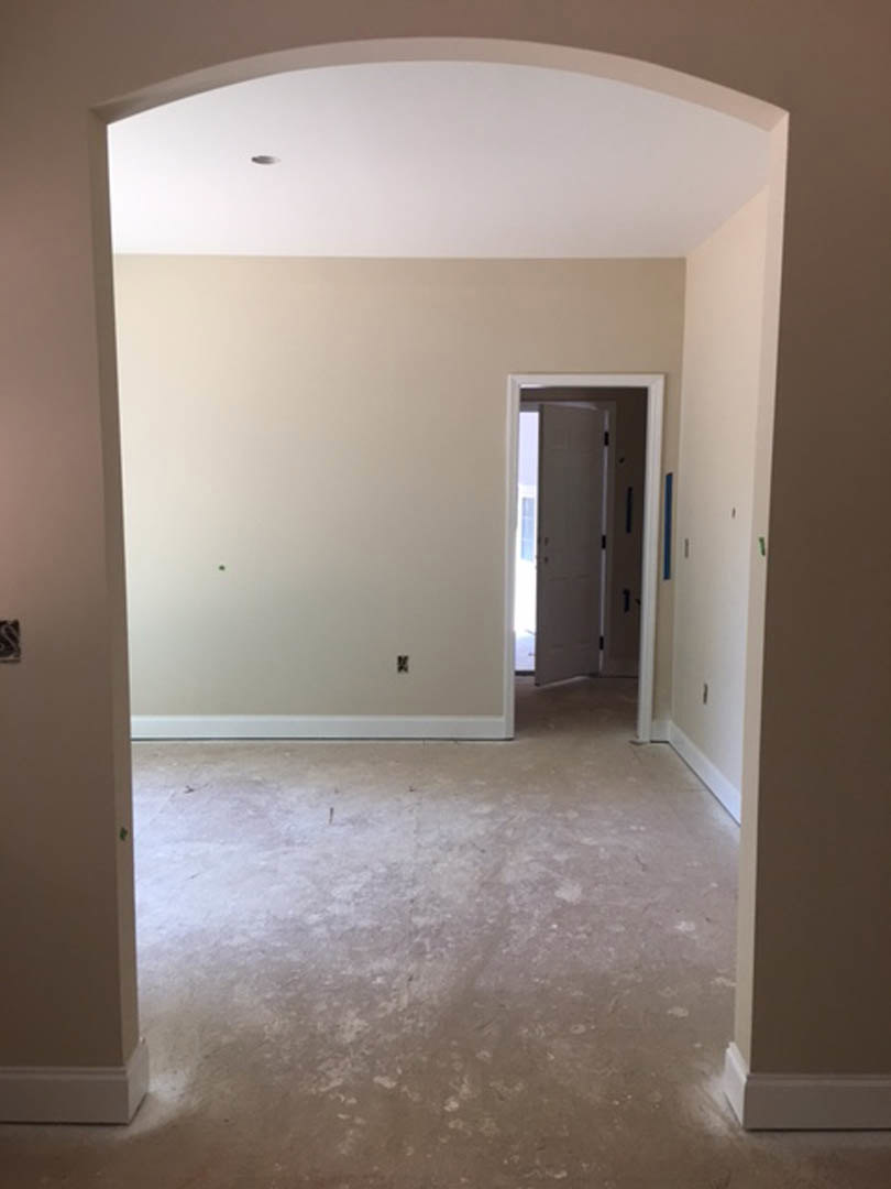 White-painted hallway with open door featuring window, light fixture centered on white wall, dirty floor with scattered white paint, close-up of stone detail.
