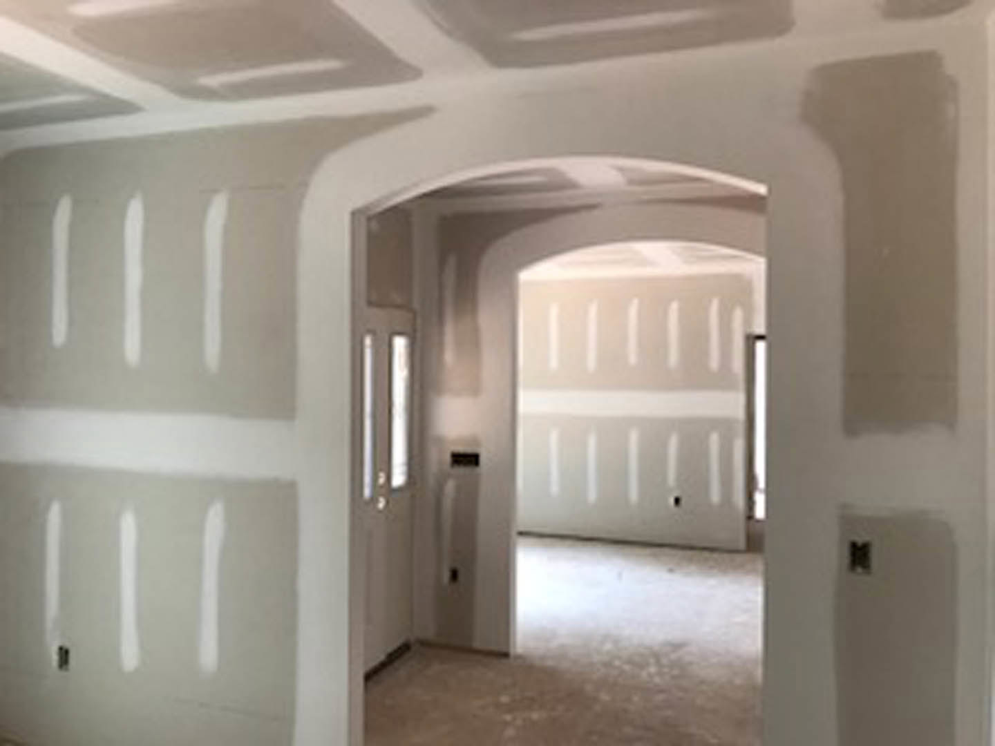 White-walled room with white ceiling, light-colored flooring, a doorway, and a black electrical outlet visible on the wall