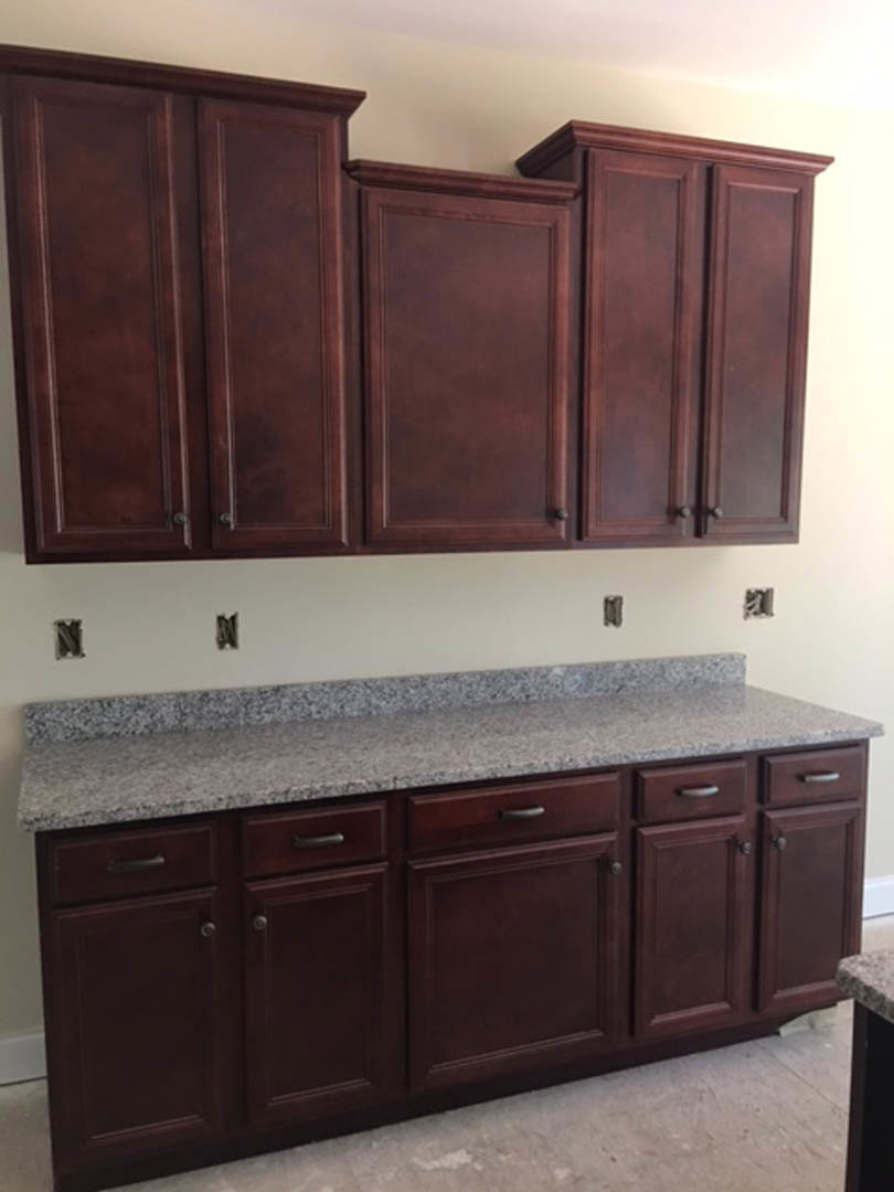 Dark wood kitchen cabinets with polished granite countertops, stainless steel appliances, and neutral tile backsplash