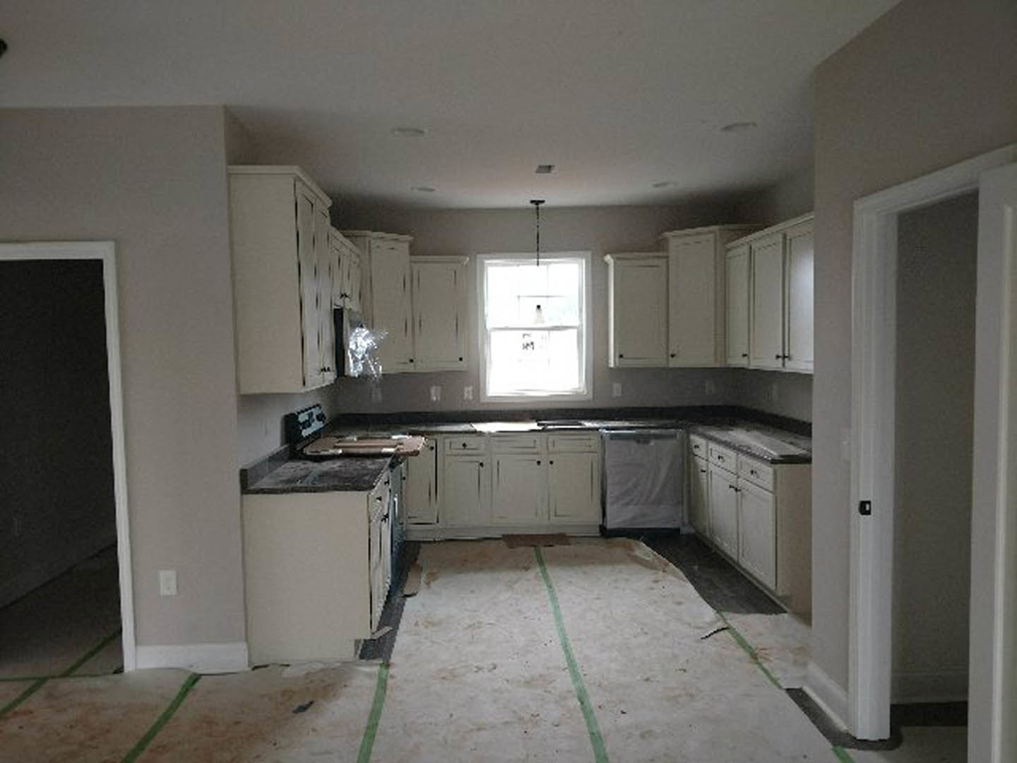 White kitchen cabinets, tile backsplash, stainless sink beneath a window with a sign, light countertops, and wood flooring