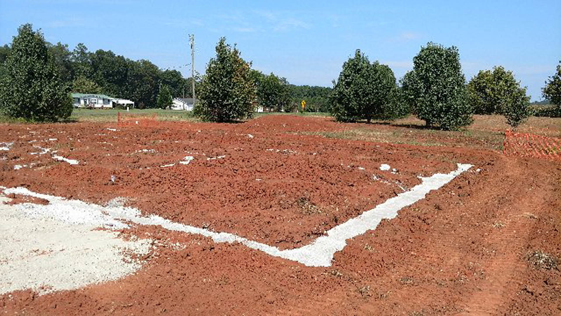 Dirt field with a white line, scattered plants, and a person walking under open sky