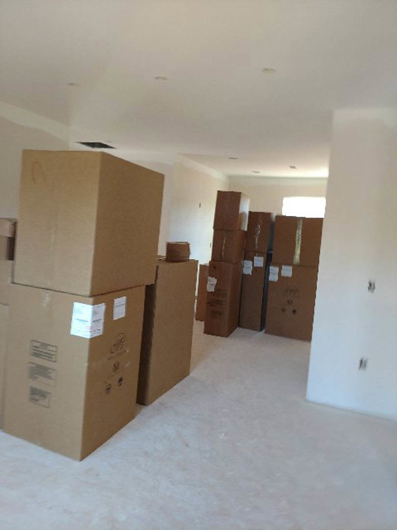 Cardboard moving boxes stacked across hardwood floor in a white-walled room with recessed ceiling lights