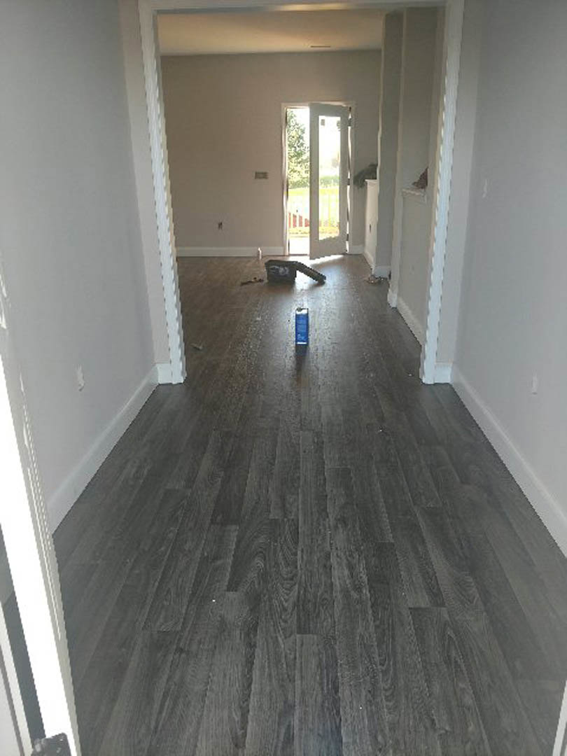 Hardwood floor with a metal can placed near a white wall, white door frame and handle visible, vacuum cleaner in the background