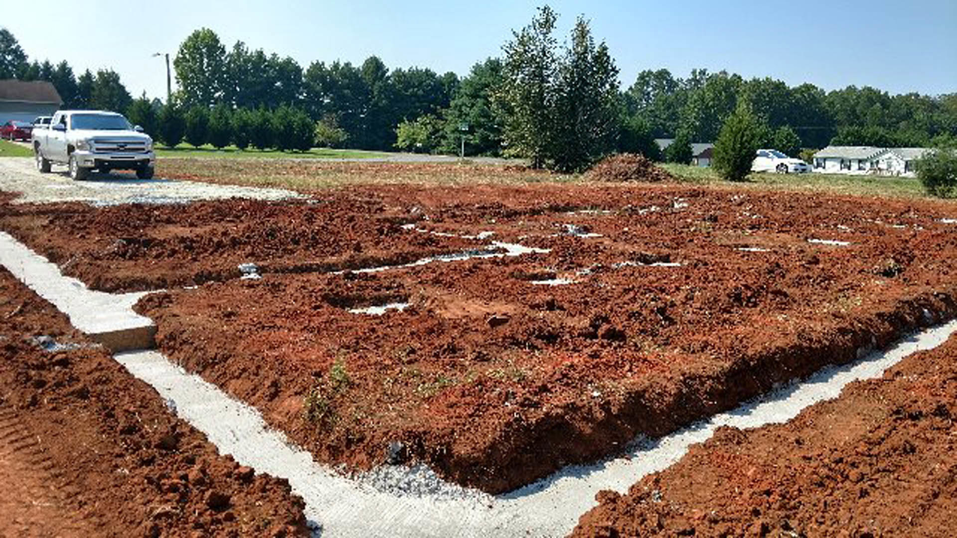 Dirt field bordered by trees, white truck with person in back, blurry car and street light in foreground