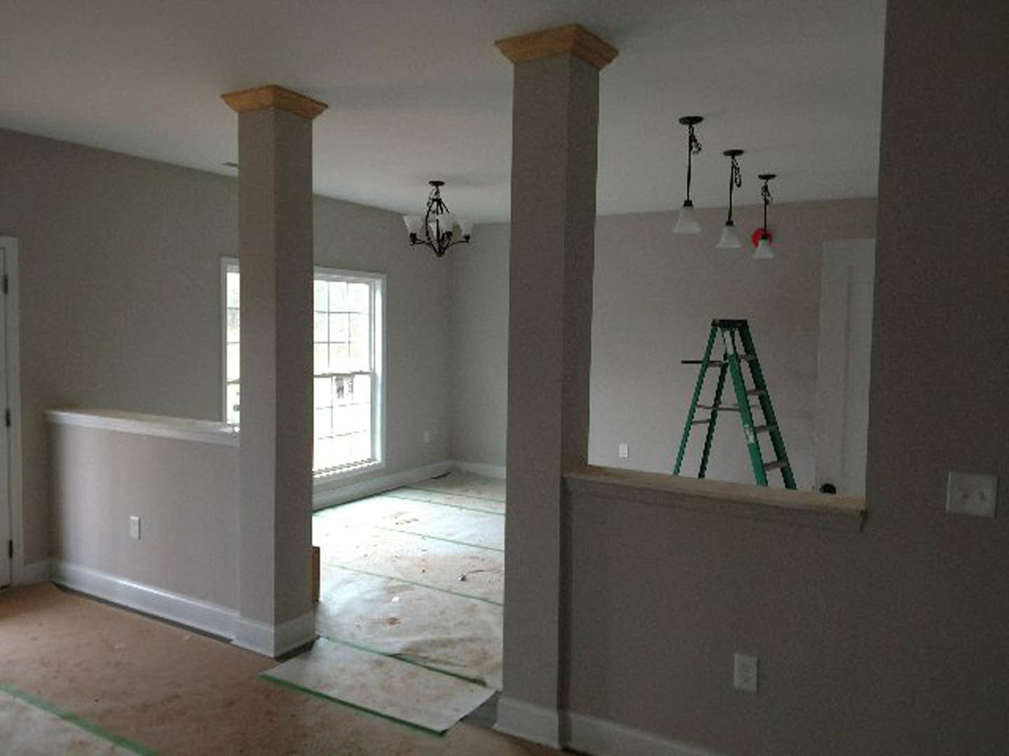 Open living space with light plaster walls, wood flooring, and two ladders positioned near a doorway and against the far wall