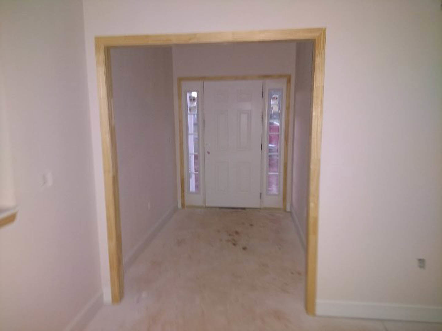 Carpeted hallway with a white door featuring glass windows, white walls, ceiling molding, and a window with a sheer white curtain