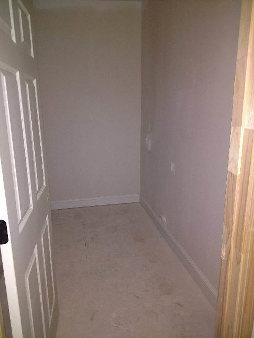 Hallway with white walls and molding, open door revealing adjacent room, white flooring, close-up of window and door detailing