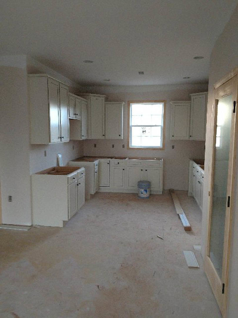 White kitchen cabinets, stainless sink, stone countertop, large window with sunlight, light-colored tile floor