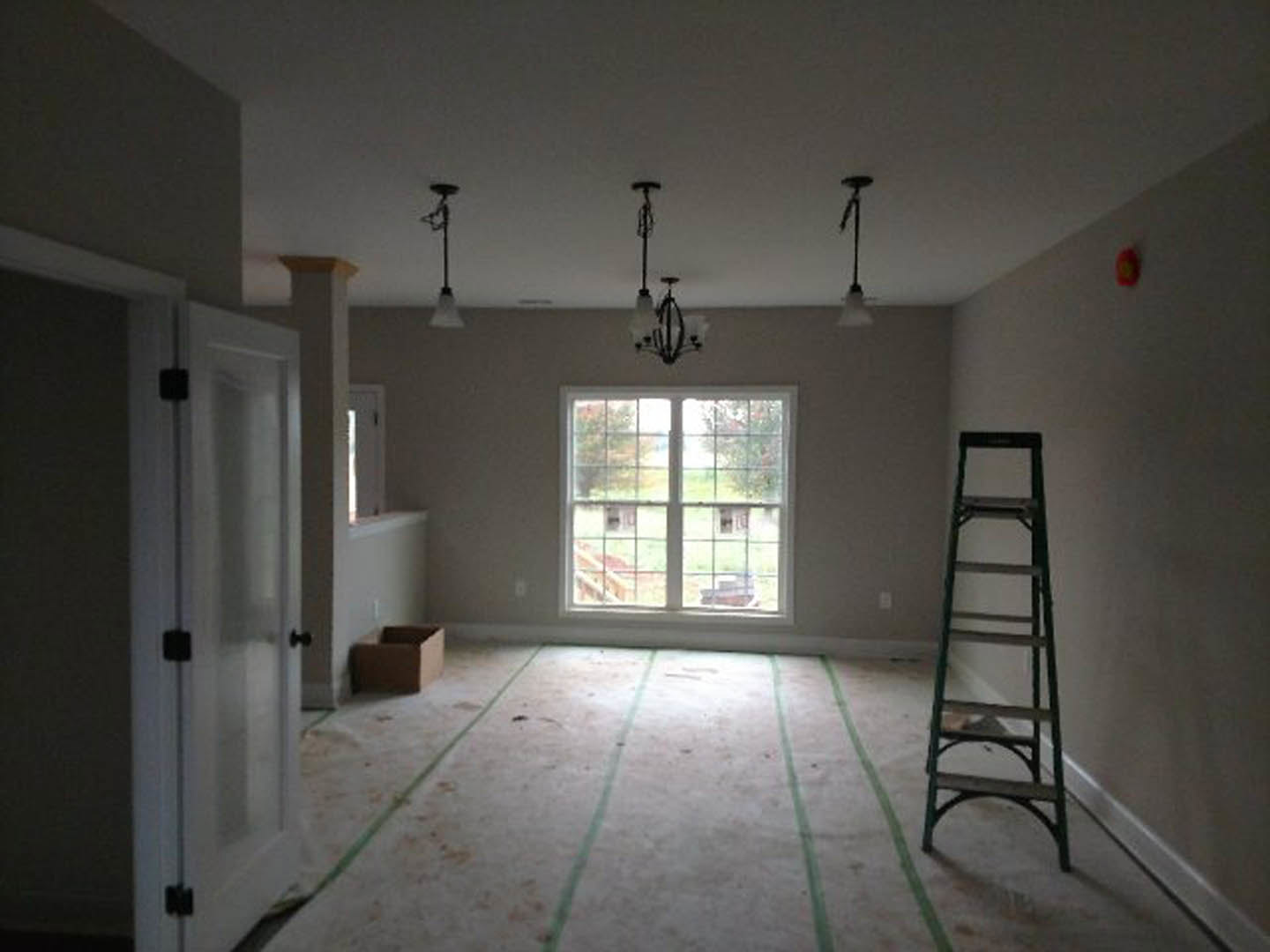White plaster walls and ceiling, wooden ladder leaning against wall, green-lined flooring, large window with outdoor view, brown box on white table, close-up of white door.