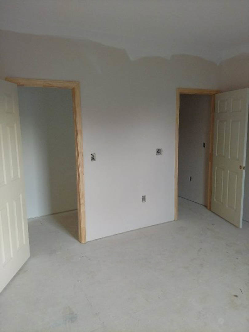 White walls with square windows, white door featuring a gold handle and wooden frame, light flooring