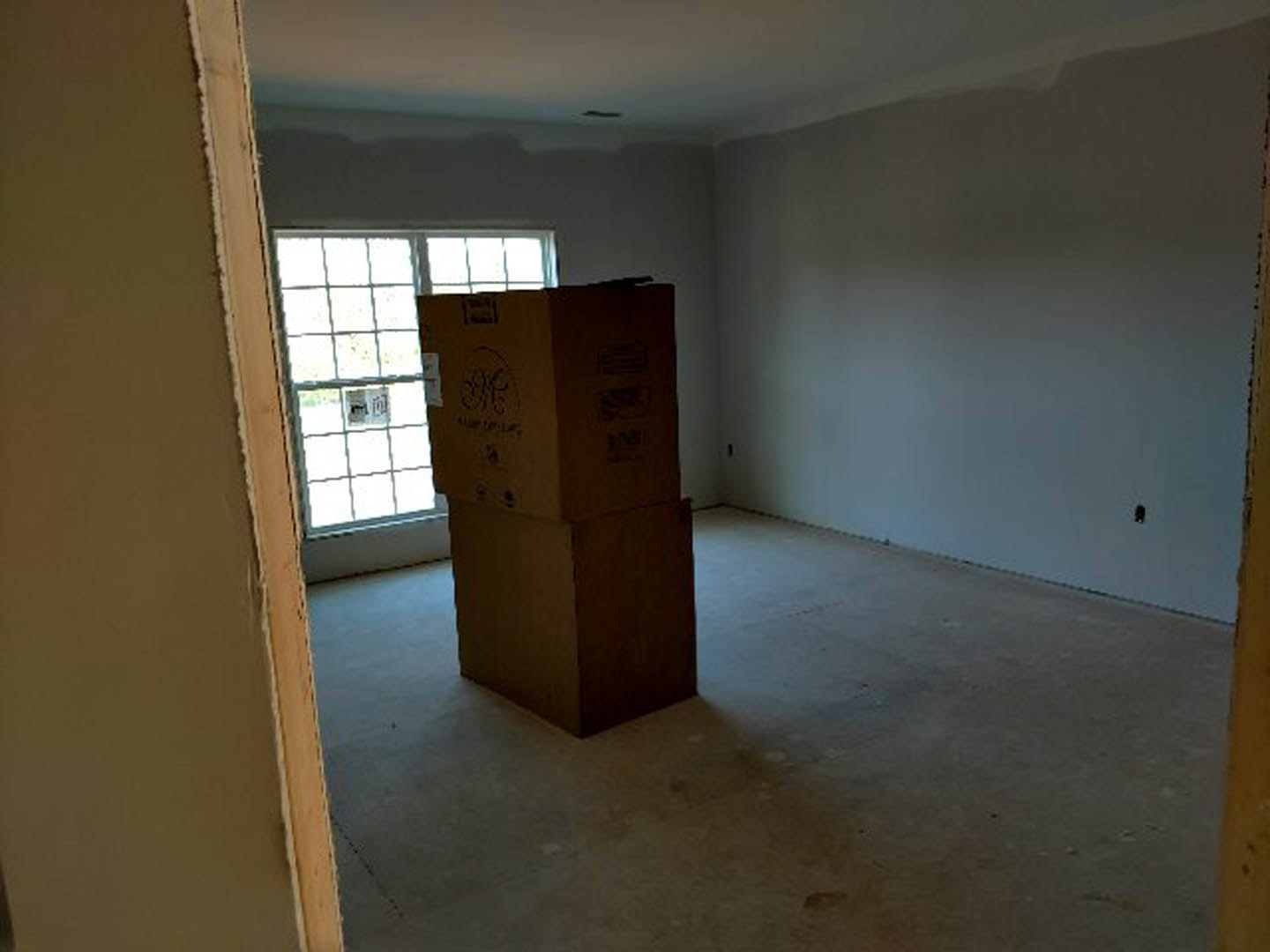 Unfurnished room with concrete floor, plaster walls, wood-framed window, and two cardboard boxes placed near the window