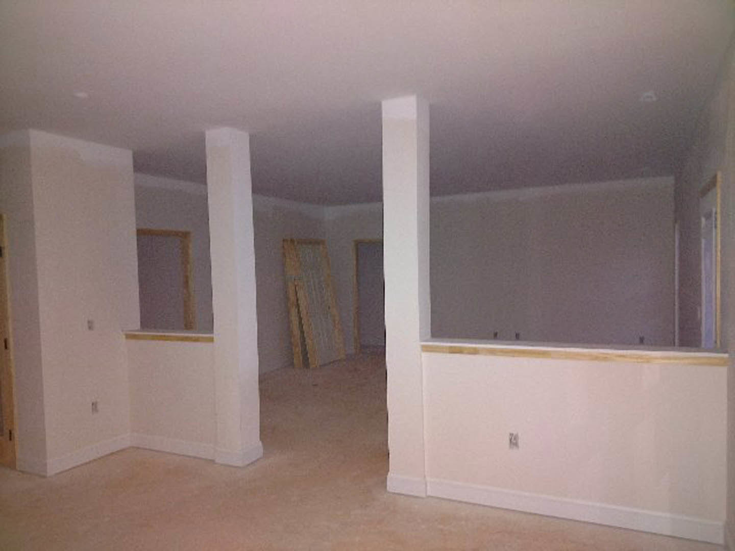 White-walled room with white ceiling, wood trim along the base, white pillar featuring a black stripe, and close-up of wooden flooring.