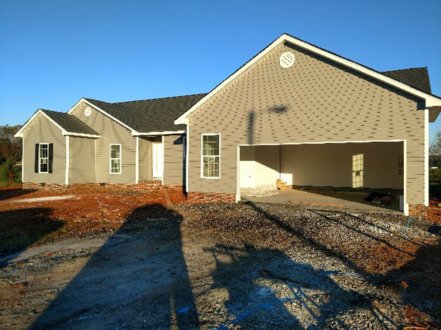 Partially built brick house with white-framed window, attached garage, and light pole casting shadow across unfinished exterior and roof