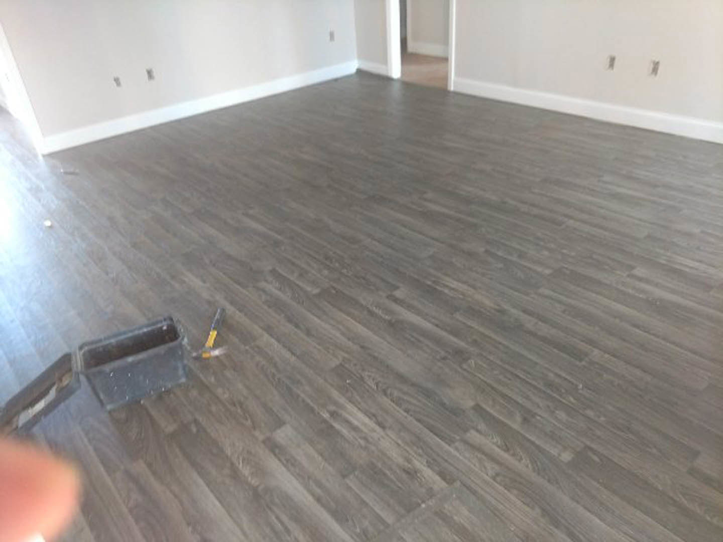 Wood plank floor with a metal toolbox and hammer placed near a white wall with electrical outlets