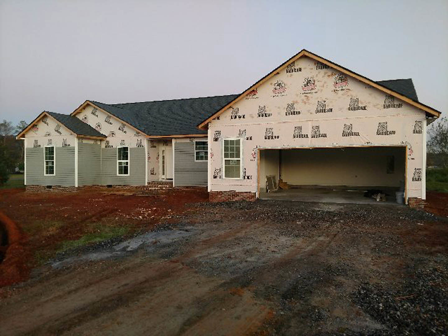 Two-story house with attached garage, white-framed windows, brick wall base, light-colored siding, and paved driveway under a partly cloudy sky